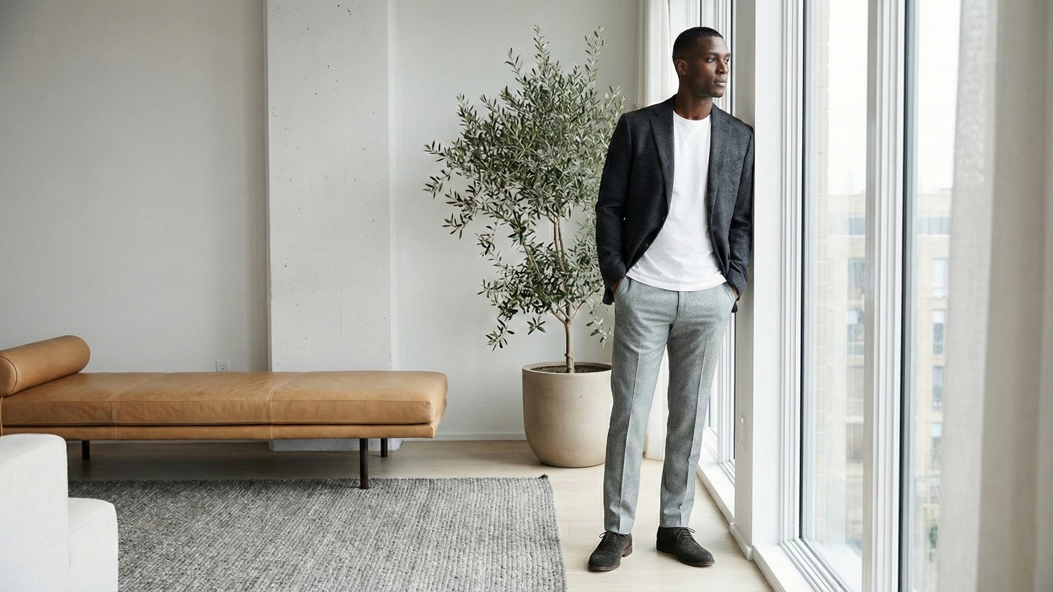Man wearing a neutral minimalist outfit with tailored trousers and blazer in a bright modern interior, representing refined minimalist men’s style.